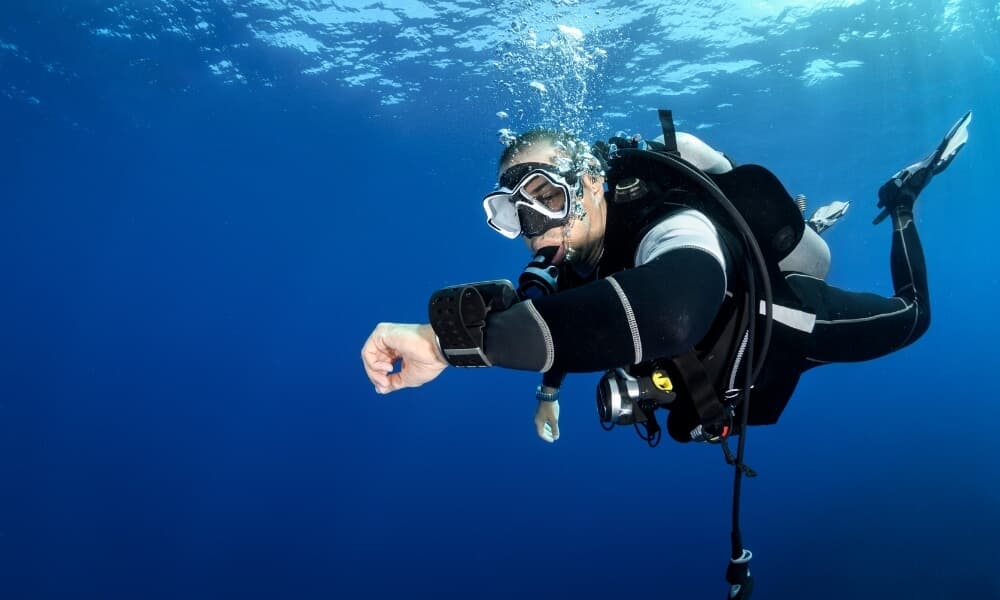 A diver in open blue water checking a dive computer