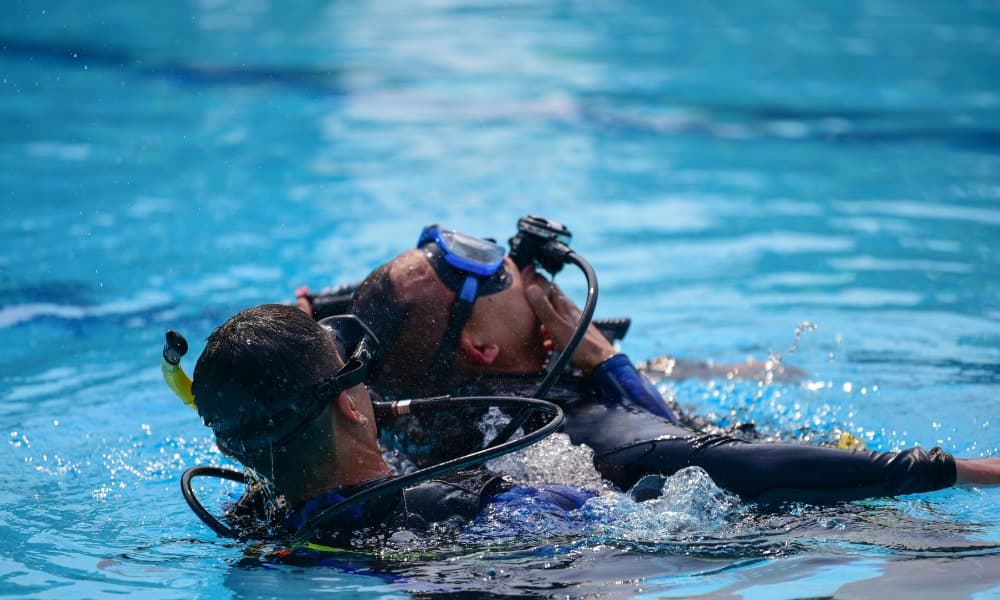 Two divers at the surface of a pool, one holding the other during a rescue exercise